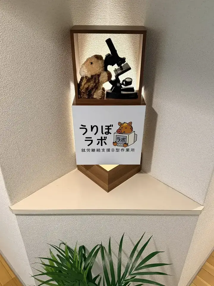 うりぼラボの入口にある、顕微鏡をのぞくうりぼのぬいぐるみとロゴパネル